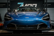 A sleek, blue sports car is prominently displayed in a showroom, showcasing its aerodynamic design and modern features.