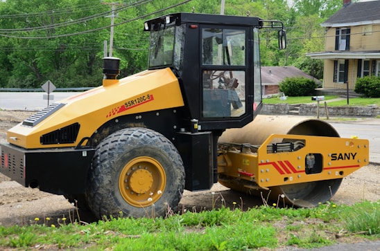 A sturdy tandem vibratory roller compacting freshly laid asphalt on a sunny construction site.