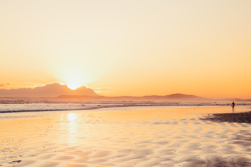 a person walking on the beach at sunset