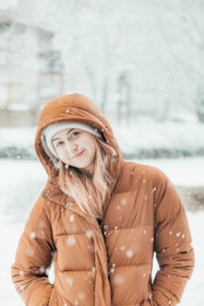 a woman standing in the snow wearing a brown jacket