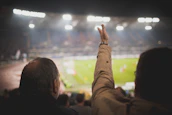 Two adults cheering at an exciting Caribbean sports event under bright stadium lights.