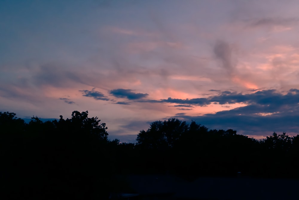 a sunset with clouds and trees in the background