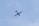An airplane is flying in the sky, with a skydiver descending nearby, set against a clear blue sky.