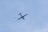 An airplane is flying in the sky, with a skydiver descending nearby, set against a clear blue sky.