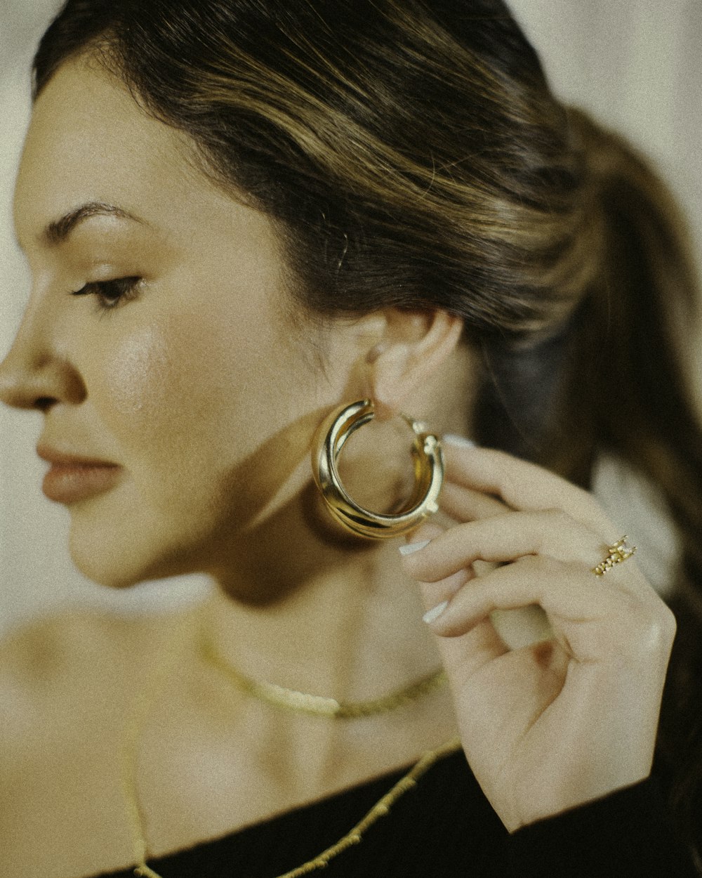 a woman in a black dress holding a pair of gold hoop earrings