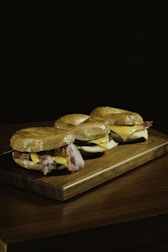 A freshly made bagel sandwich with melted cheese, eggs, and greens on a rustic wooden board.
