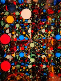 The image contains a dense array of multicolored circles in various sizes, arranged in a seemingly infinite pattern. The circles are of vibrant colors including red, blue, yellow, and green, set against a black background. The arrangement creates a kaleidoscopic visual effect, giving an impression of depth and complexity.