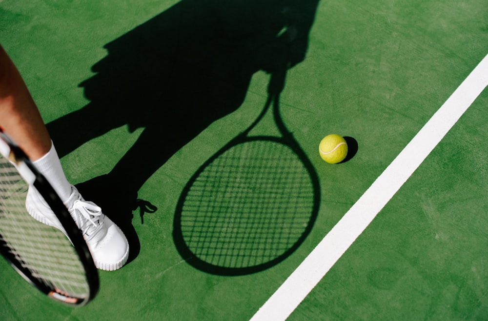 uma sombra de uma pessoa segurando uma raquete de tênis e uma bola de tênis