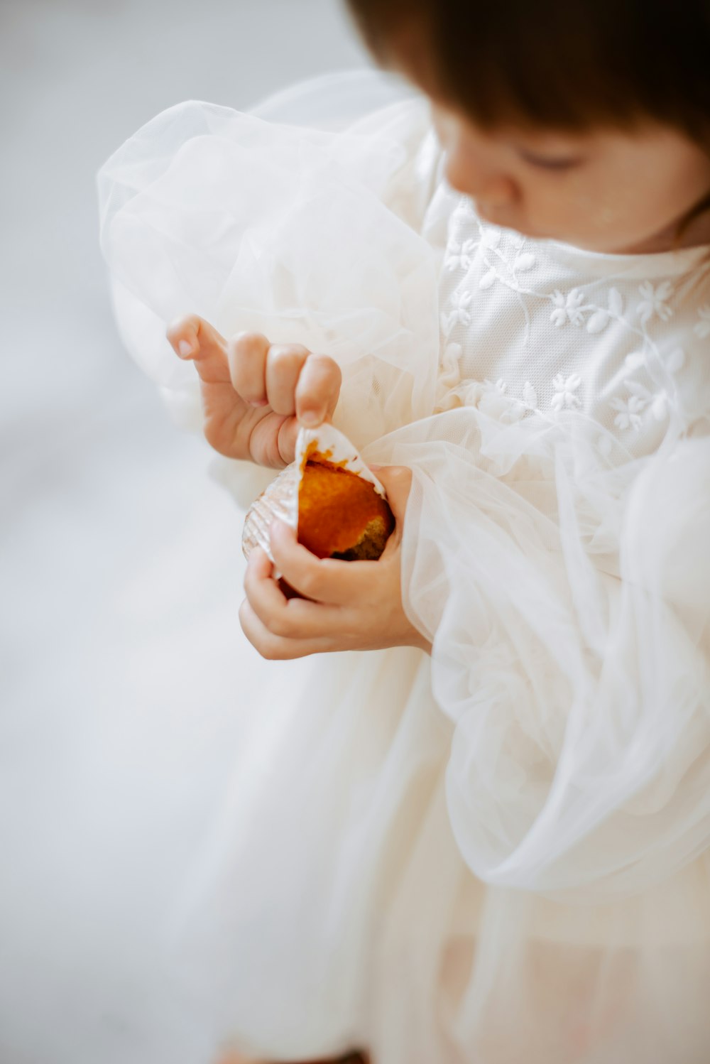 a little girl in a white dress holding a piece of food
