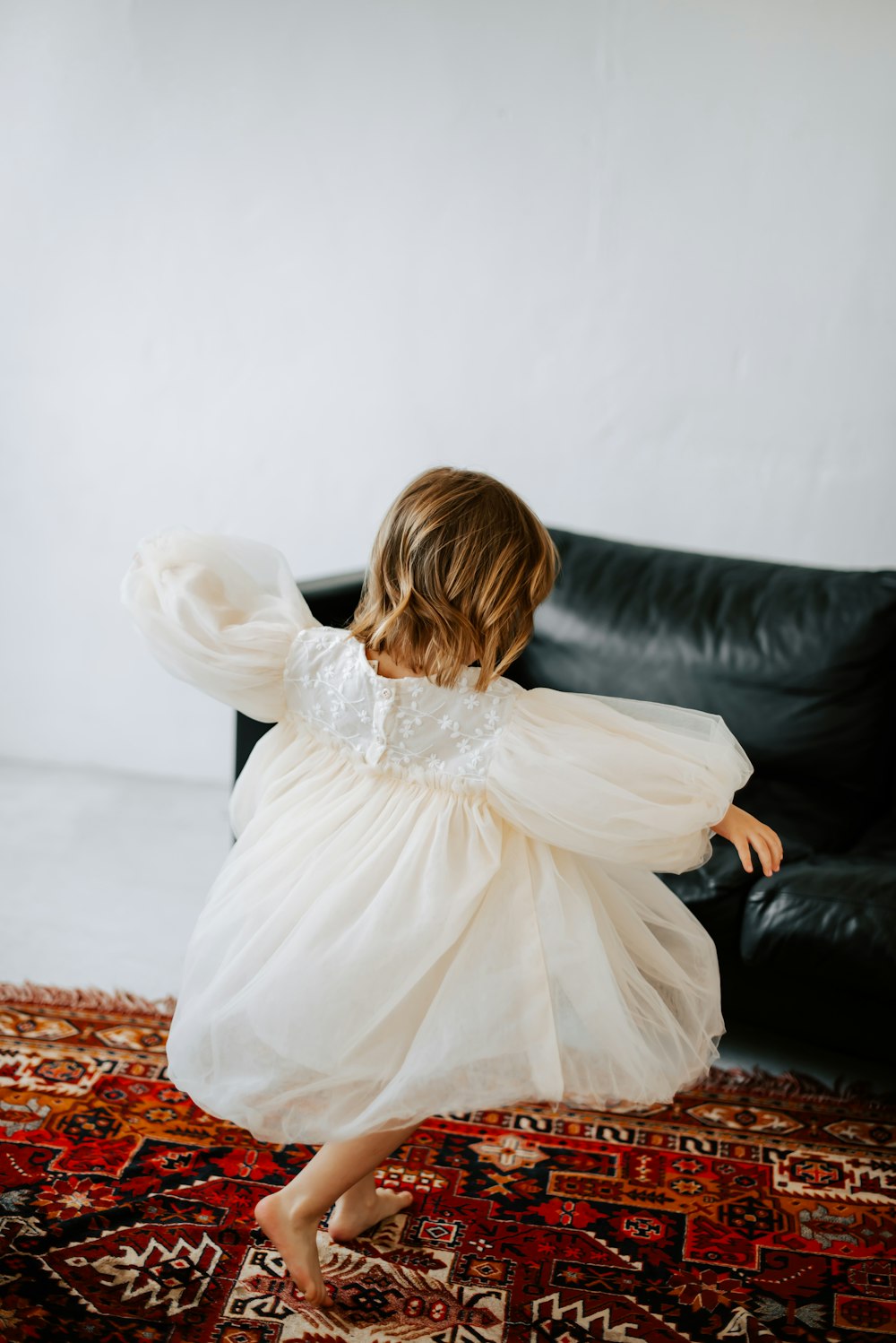 a little girl in a white dress standing on a rug