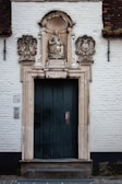An old stone doorway with an intricately carved archway featuring a statue of a crowned woman holding a child. The plaque below reads 'H. MARIA BVG' and 'ANNO 1634'. The building has a brick wall with a visible number '7/9' on the left side.