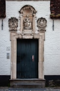 An old stone doorway with an intricately carved archway featuring a statue of a crowned woman holding a child. The plaque below reads 'H. MARIA BVG' and 'ANNO 1634'. The building has a brick wall with a visible number '7/9' on the left side.