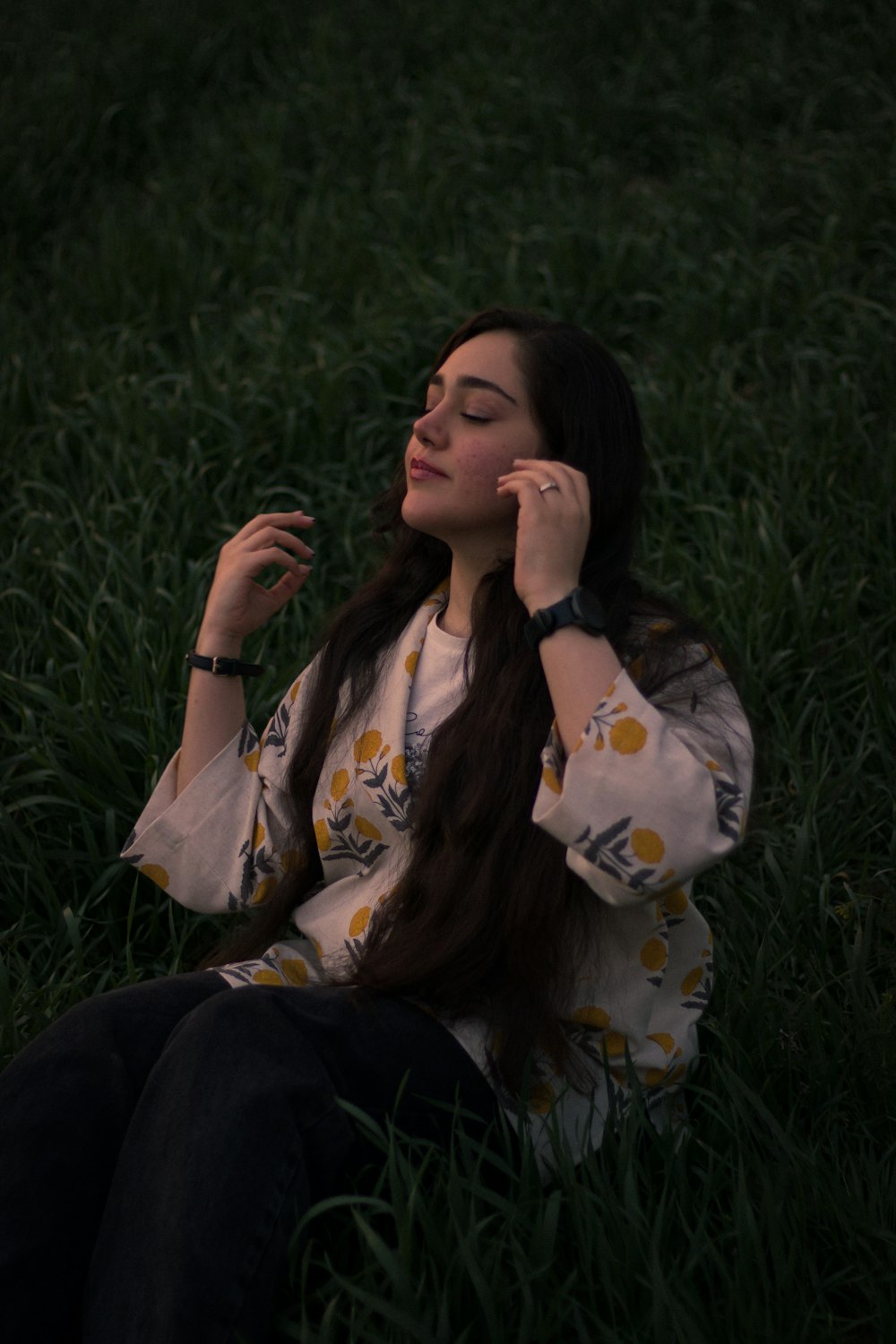 a woman sitting in the grass talking on a cell phone