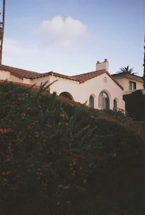 Front view of a charming Andalusian villa with white walls and terracotta roof tiles under a bright blue sky.