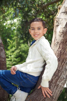 A cheerful young boy from Killarney sitting under a tree, smiling with a notebook in hand.