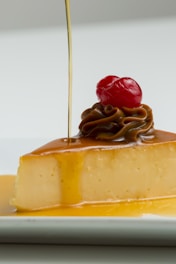 A hand holding a slice of flan with caramel dripping slowly onto a white plate.