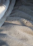 A close-up of a soft green throw blanket draped over a chair near a window with natural light.