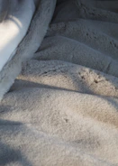 A close-up of a soft green throw blanket draped over a chair near a window with natural light.