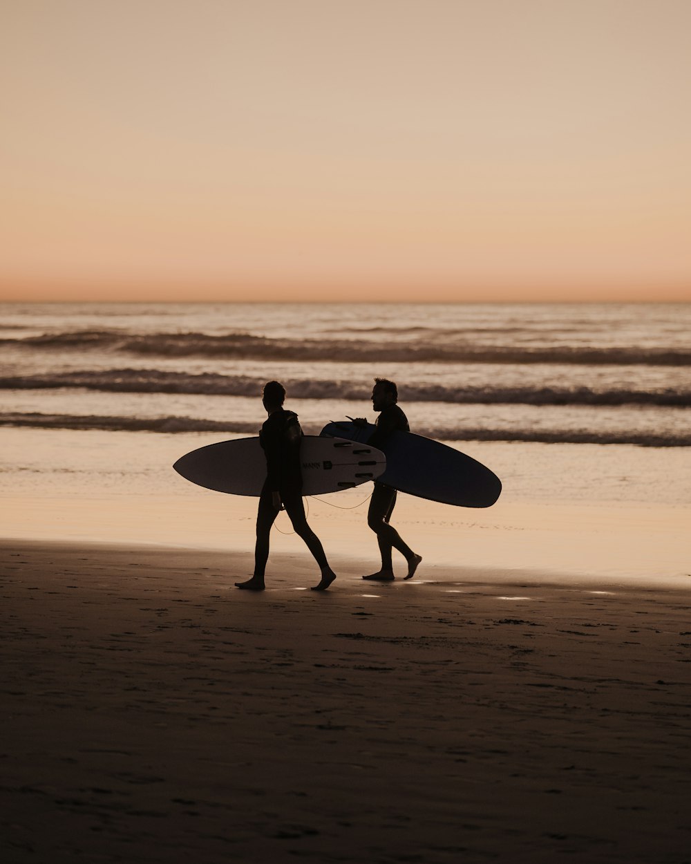 two people walking on a beach with a surfboard