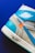 A close-up of a stylish sneaker, featuring turquoise and cream colors with an orange accent. The sneaker displays the word 'AIR' on the midsole and a visible logo with wings on the upper part.
