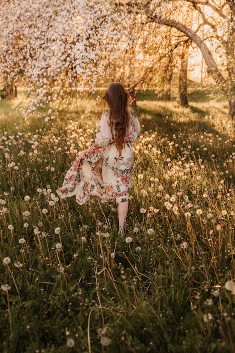 A model wearing a light, floral bohemian dress standing in a sunlit meadow.