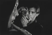 An atmospheric black-and-white portrait of Augustin Le Prince beside an early motion picture camera.