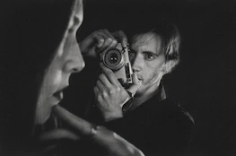 An atmospheric black-and-white portrait of Augustin Le Prince beside an early motion picture camera.