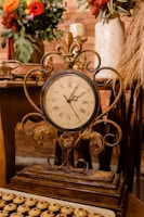 Vintage brass clock with ornate details resting on a rustic wooden table.