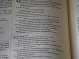 A close-up view of an open book, revealing printed text in columns. The text includes a conversation and some questions posed, with a section titled 'God’s answer.' The page has large and small font sizes and is displayed at an angle, adding depth and focus.