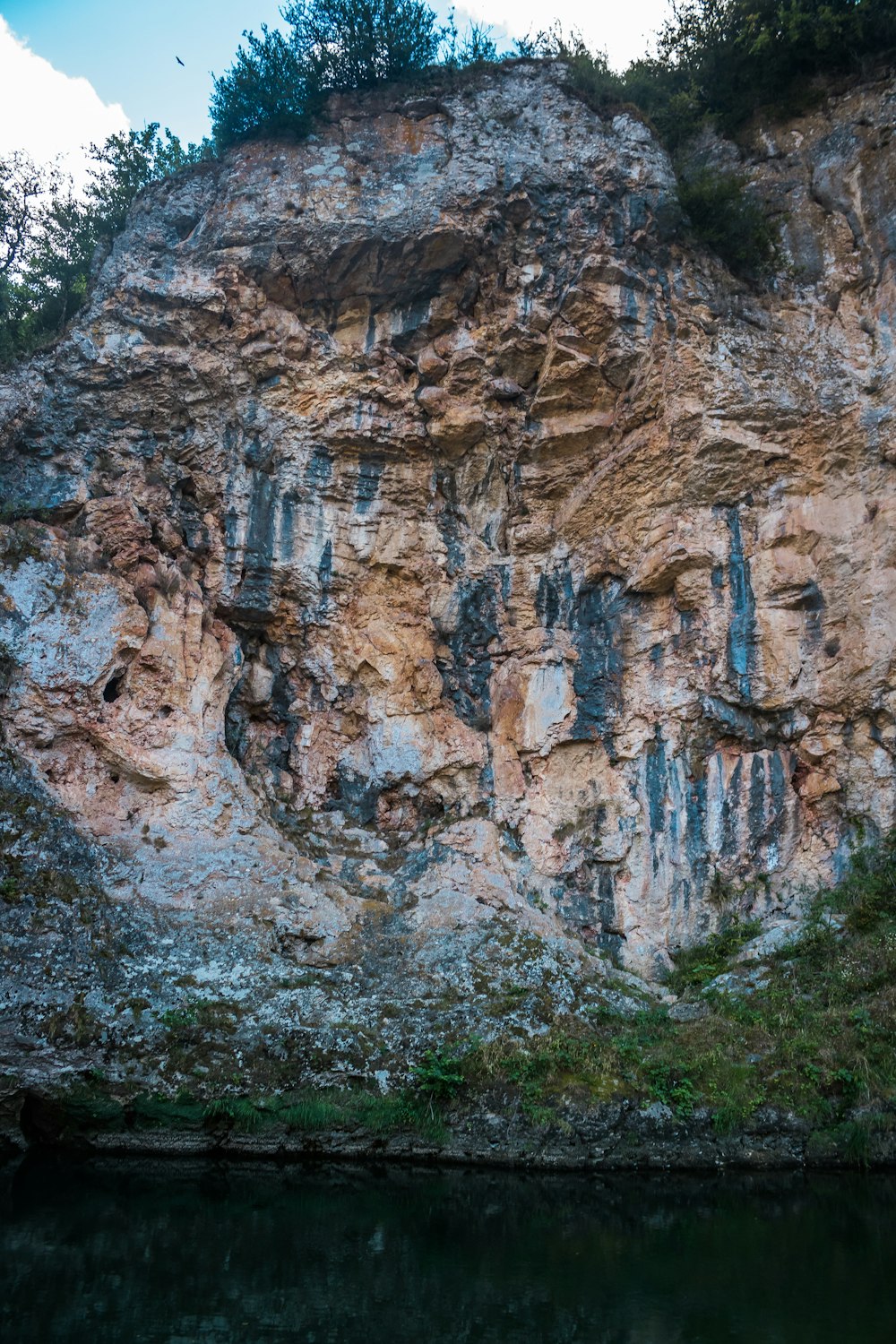 una grande parete rocciosa con un piccolo specchio d'acqua di fronte