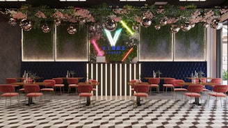 A modern lounge interior featuring geometric floor tiles, pink chairs with gold legs, and wooden tables. The back wall is adorned with vertical neon lights and lush greenery, including pink flowers. Disco balls hang from the ceiling, adding a festive touch.