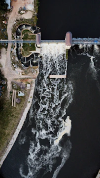 Aerial shot of a dam with water flowing and construction equipment nearby.
