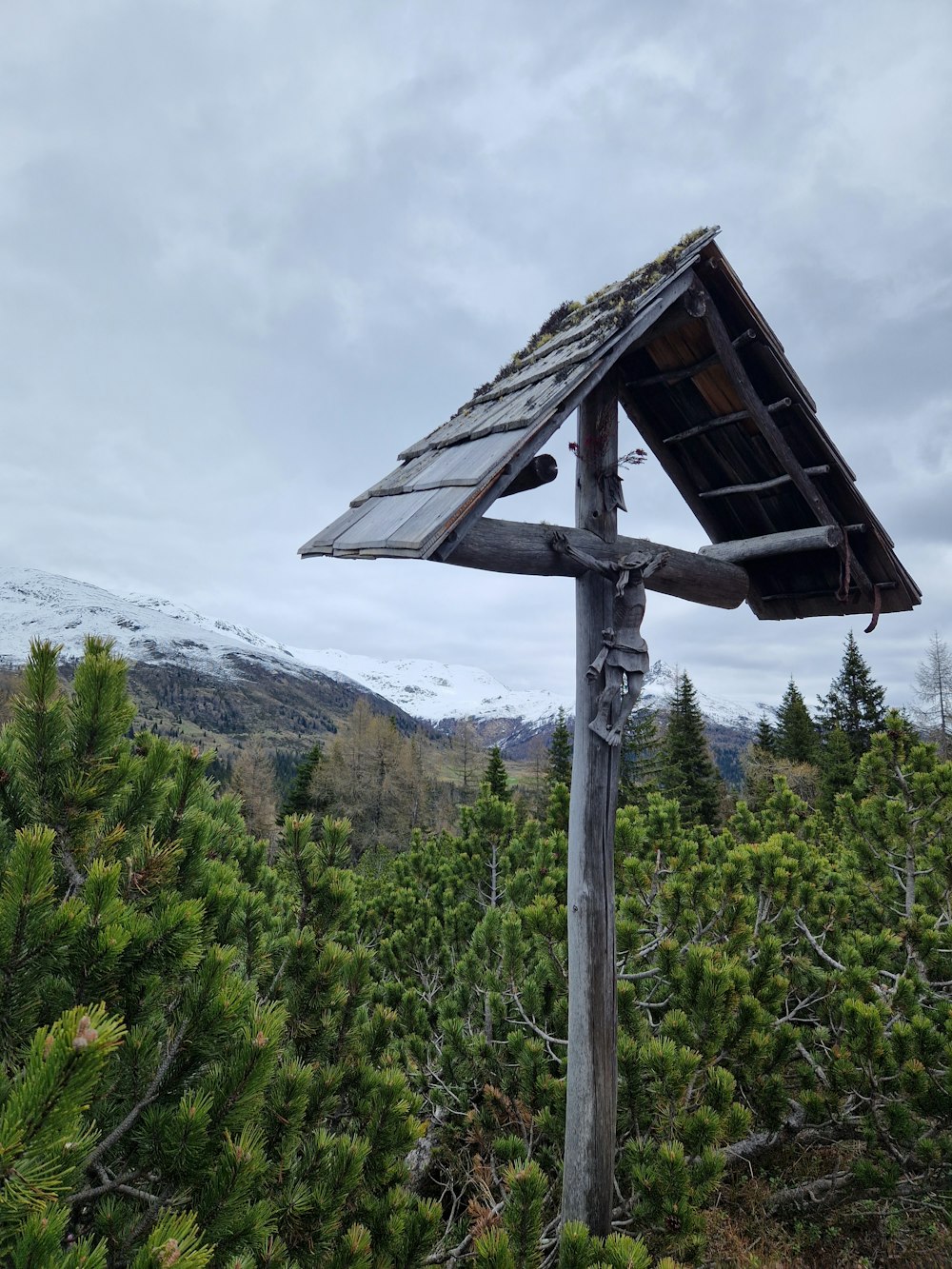 a wooden pole with a wooden roof and a snow covered mountain in the background