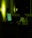 A person sits at a desk in a dimly lit room, writing on a notepad. The scene is illuminated by the greenish glow of a computer screen and a soft light on the wall. Papers are pinned to the wall and the room appears quiet and focused.