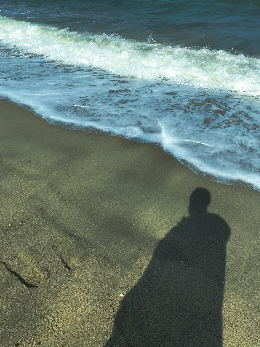 a shadow of a person standing on a beach next to the ocean