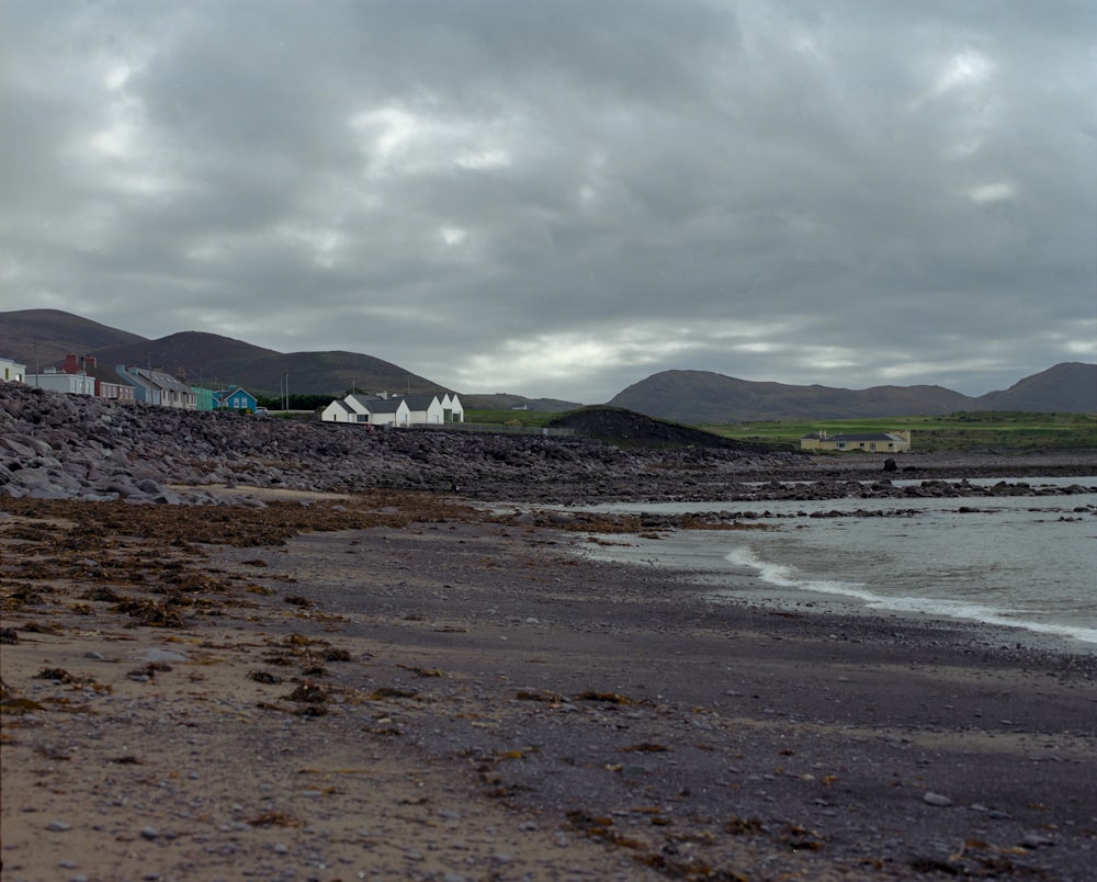 a beach with houses on the shore and mountains in the background