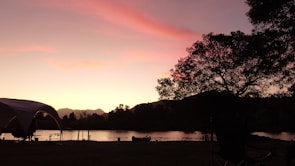 A vibrant sunset over a quiet lakeside campsite where art supplies are set up.