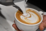 Close-up of a barista pouring latte art into a ceramic cup.