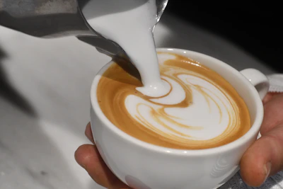 Close-up of a barista pouring latte art into a ceramic cup.