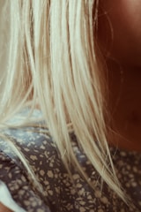 Blonde hair cascades over the shoulder, contrasting with a fabric featuring a blue and white floral pattern. The lighting creates a warm, soft focus effect.