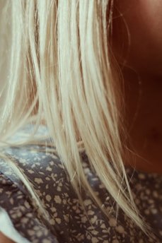 Blonde hair cascades over the shoulder, contrasting with a fabric featuring a blue and white floral pattern. The lighting creates a warm, soft focus effect.