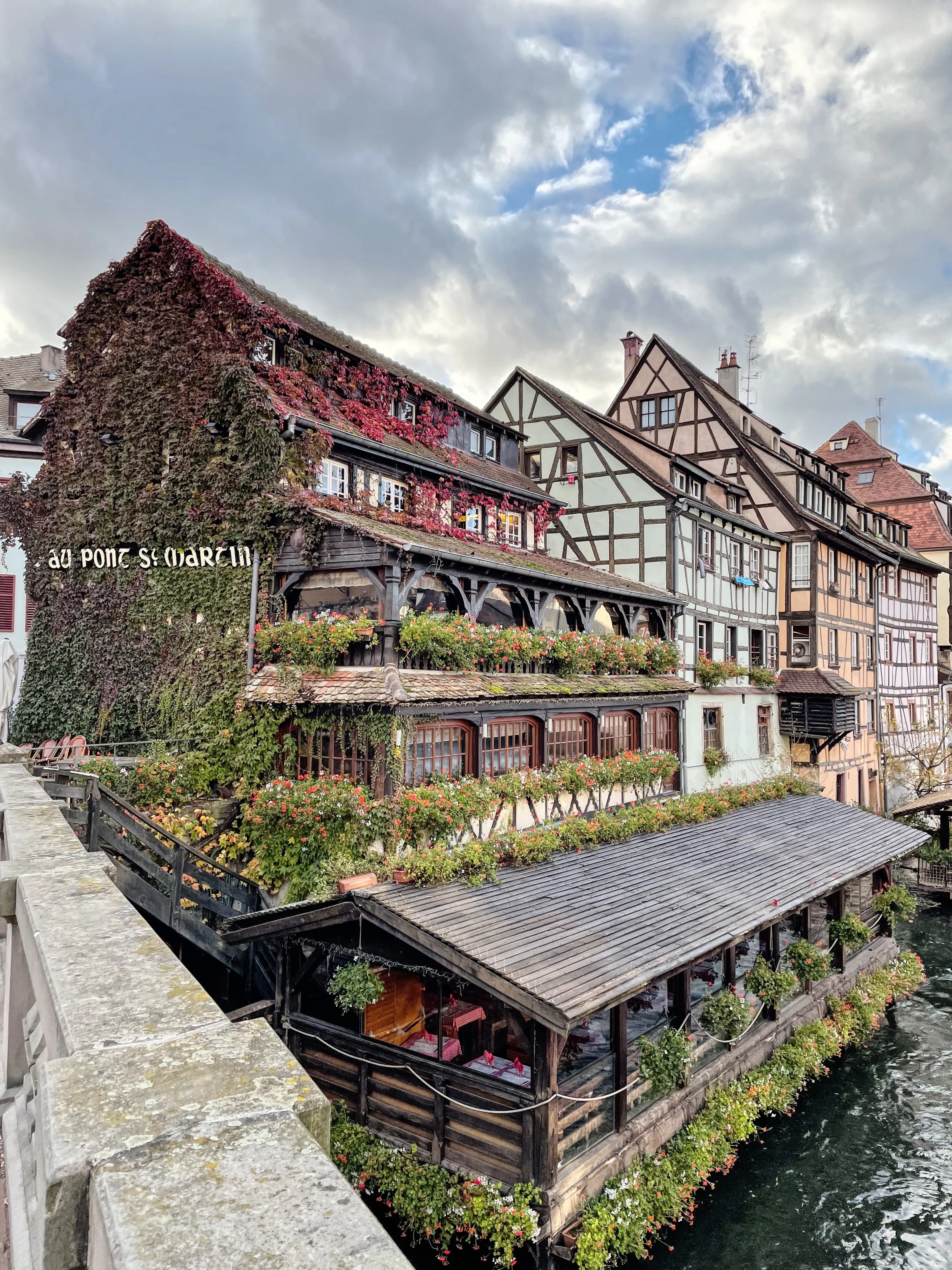 The ivy-covered Au Pont St Martin restaurant and its wooden boathouse sit on a canal amid autumn colour.