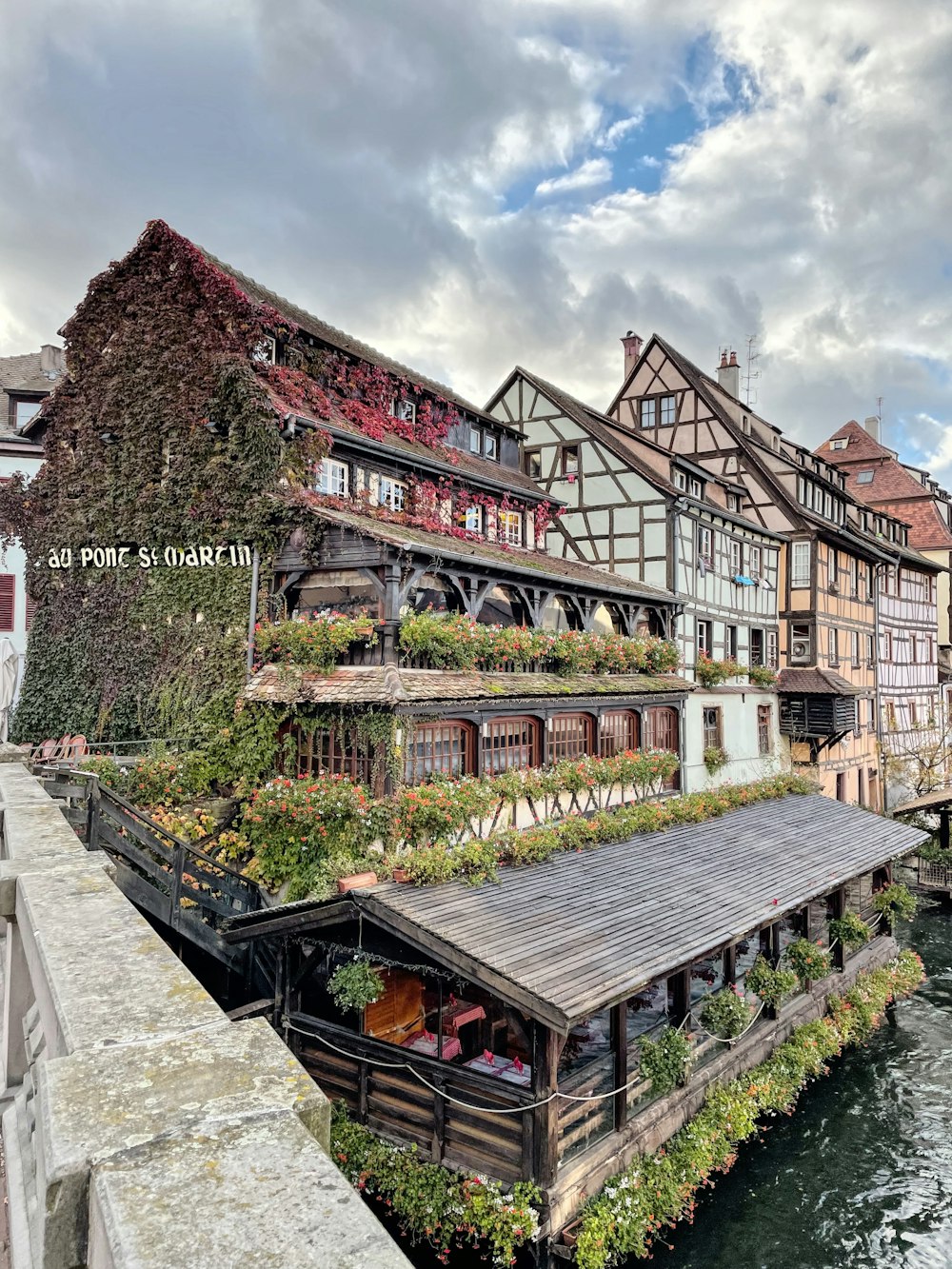 a river runs past a row of buildings with plants growing on them