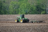 A tractor moving through rich soil with workers nearby.