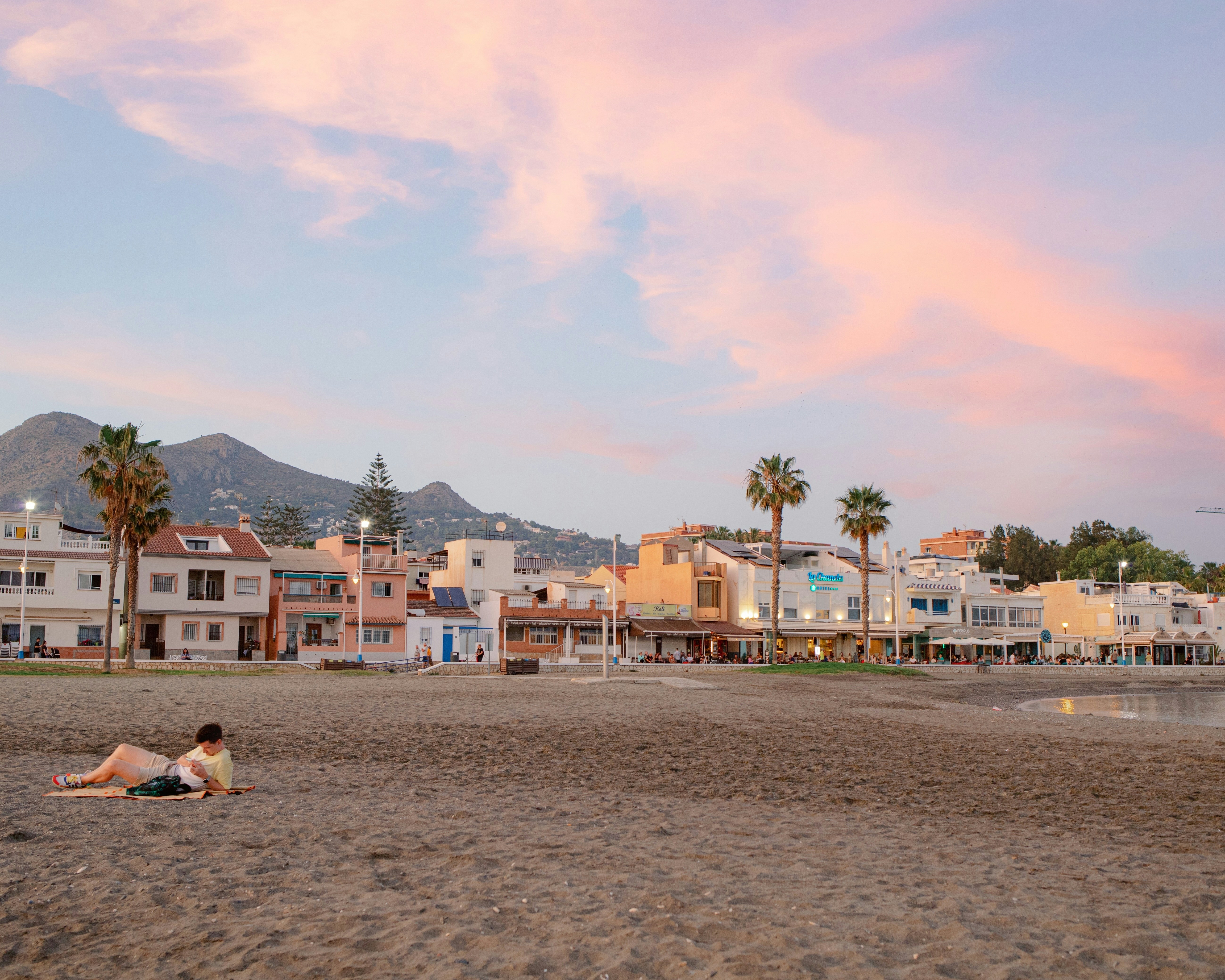 7 Underrated Beach Towns Where Your Money Goes Further – a couple of people laying on top of a sandy beach