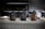 Three handguns are securely placed in leather holsters on a grid-patterned surface. Each holster is uniquely designed with stitching details and distinct patches, including a cross on the left holster. The background includes shelves with various items, out of focus, in a workshop-like setting.