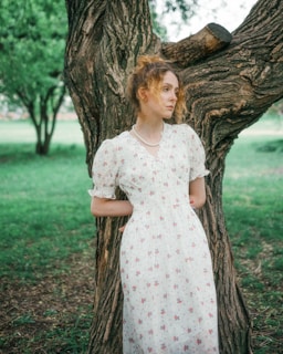 a woman in a white dress standing next to a tree