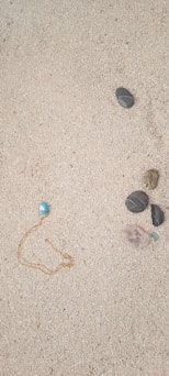Sunlit outdoor scene showing a necklace resting on textured sand with terracotta tones.