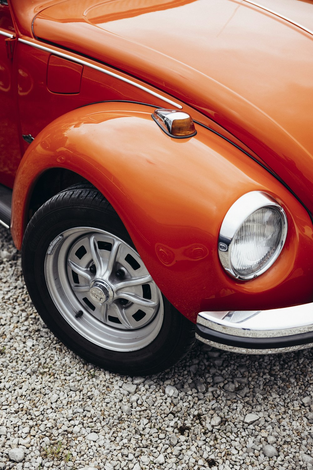 an orange vw bug parked on a gravel road