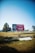 A large billboard stands in an open, grassy area under a clear blue sky. The billboard features a Coca-Cola advertisement with the text 'Wishing You a Safe Journey' and some imagery. Trees and a parked car are visible in the background, adding to the spacious outdoor setting.